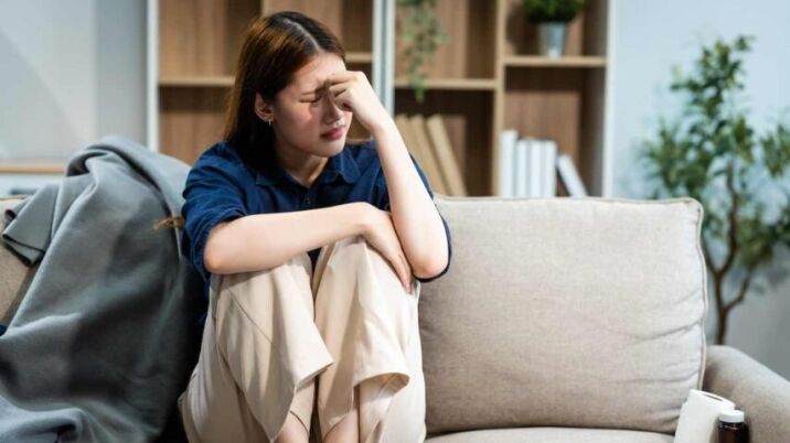 young woman sits on a sofa struggling with her intense emotions due to her borderline personality disorder